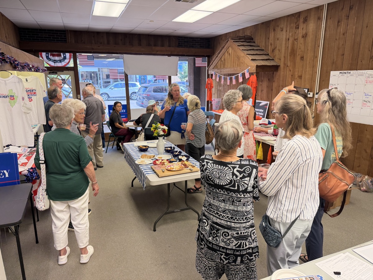 Neighbors gathered around a food table inside the headquarters, with flags and the front windows behind them