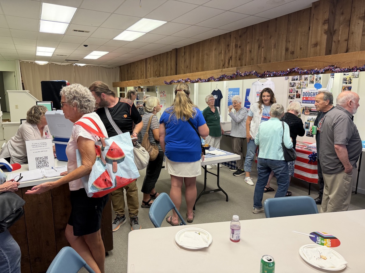 Guests signing in at a table inside the headquarters during the Open House, with campaign shirts and a candidate display along the wall behind them