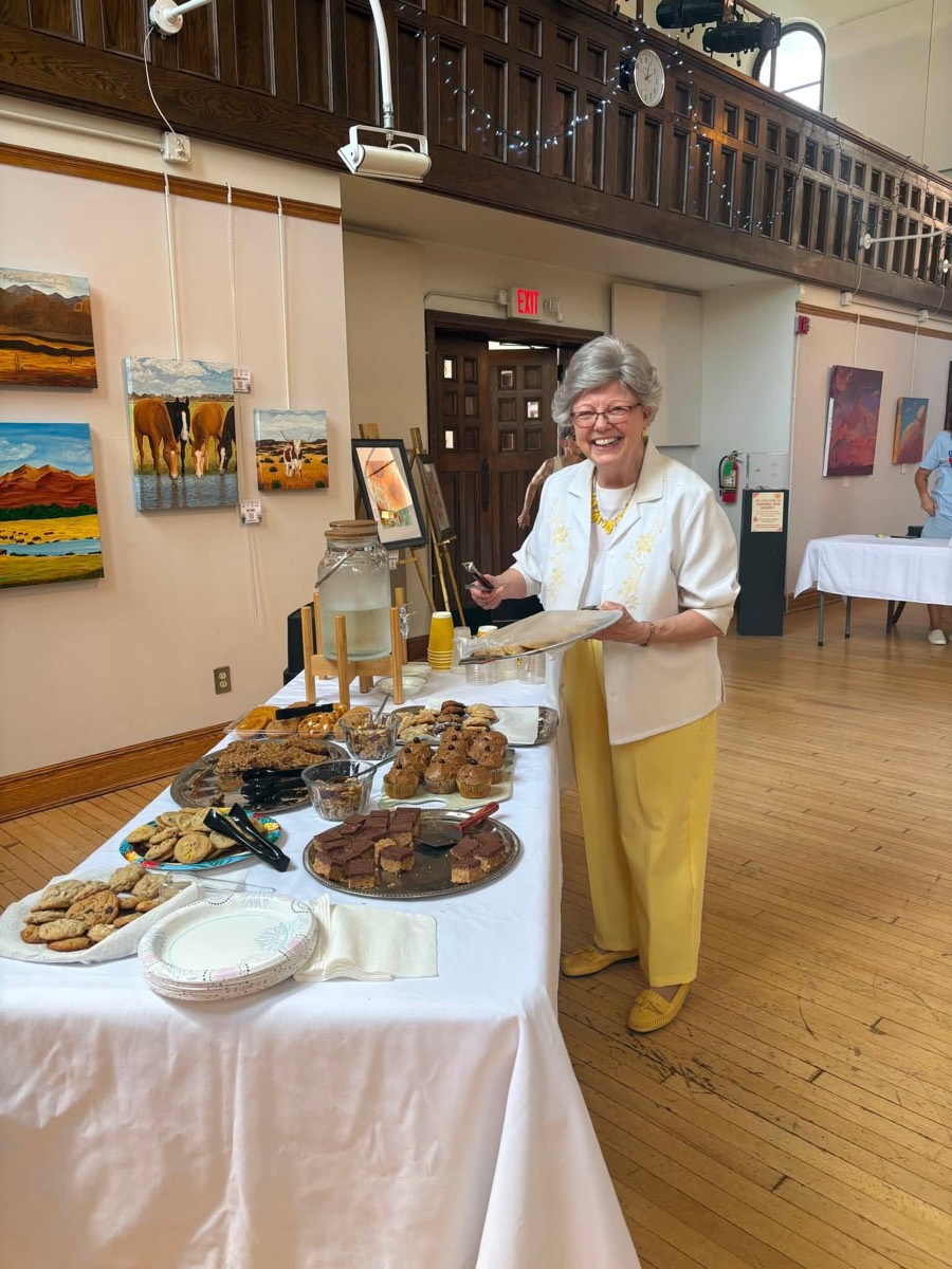 A volunteer smiling behind a long table set with plates of cookies, brownies, and muffins for the audience