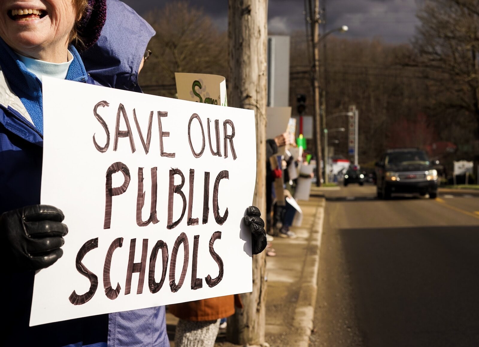 A demonstrator holding a handmade Save Our Public Schools sign