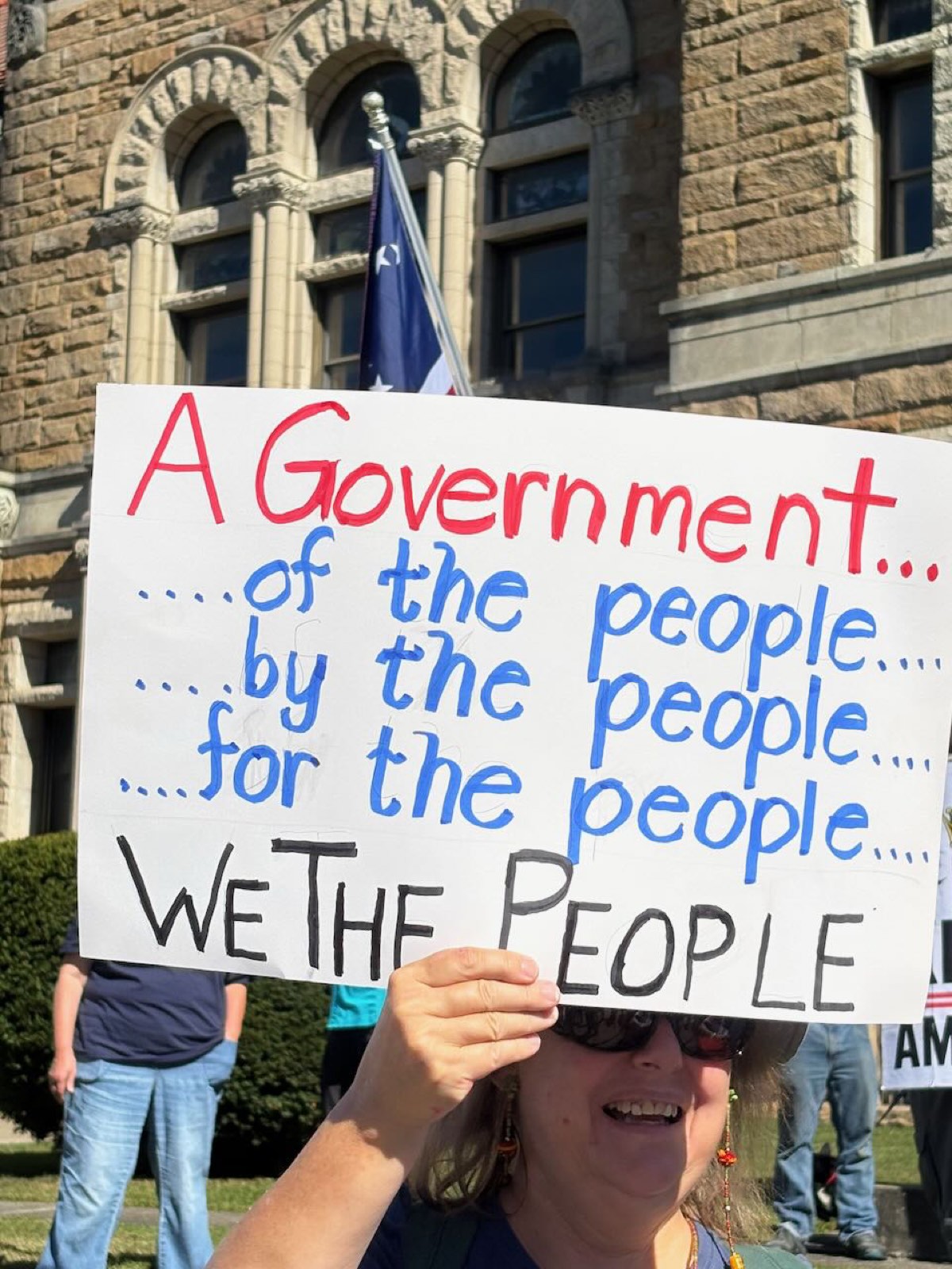A handmade sign reading a government of, by, and for the people — We the People